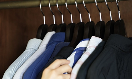 ナカタハンガー製のSET-12に掛けられた服の中から、クローゼットで服を選んでいる人の手